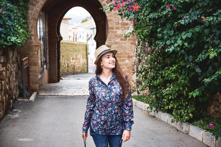 Beautiful young woman tourist in hat with camera walking in old town. Travelling concept. Castle in Denia, Spain.の写真素材