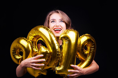 Portrait of a young funny woman with bright make-up having fun and holding golden balloons in hands...