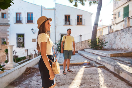Couple of tourists walking in historical quarter of Spainish town on a sunny summer day.