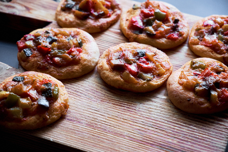 Many freshly baked mini pizzas Ñocas on wooden board. Traditional Spanish pastry with vegetables.