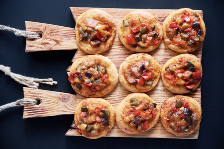 Top view of many traditional Spanish baked mini pizzas Ñocas on wooden board. Black background.の写真素材