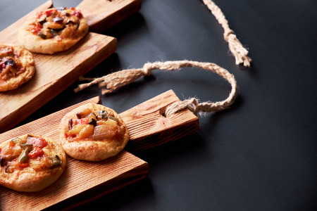 Close-up of traditional Spanish baked mini pizzas Ñocas on wooden board. Black background.の写真素材