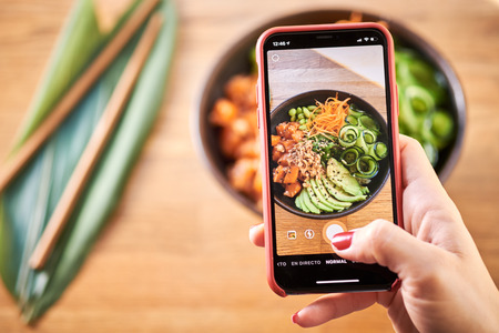 Woman taking photo of traditional Hawaiian dish poke bowl with her smart phone. Hawaiian and...