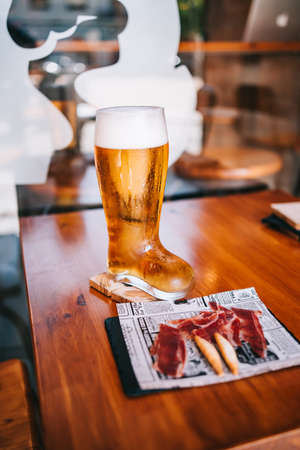 Beer glass boot with delicious spanish iberian ham snacks on a wooden tableの写真素材