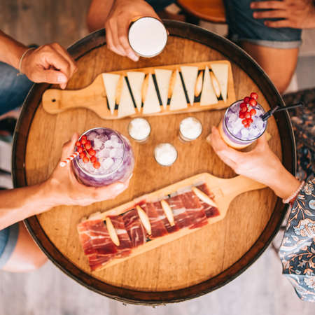 a group of friends sits on the terrace in the summer behind a wooden barrel with cocktails and a snack. Top viewの写真素材
