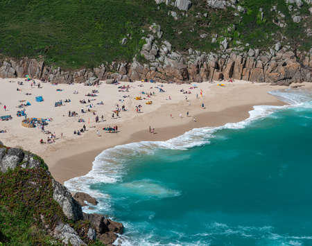 lots of people swimming and sunbathing at the blue waters at Porthcurno Beachの写真素材