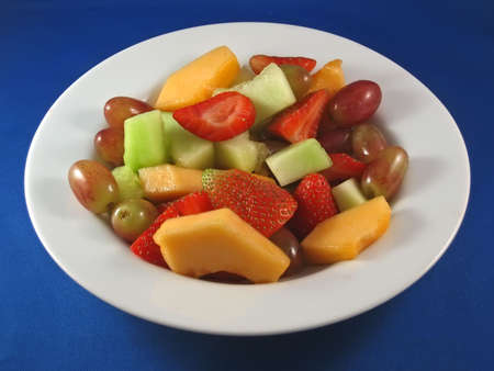 White bowl of fruit salad with strawberries, cantaloupe, honeydew, and grapes.の写真素材