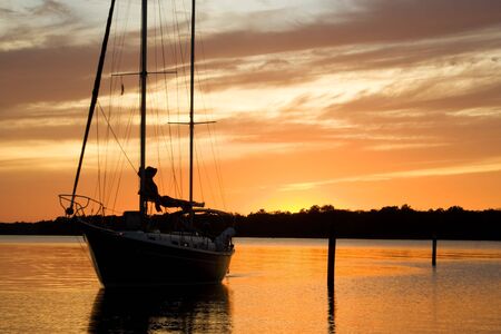 sailing yacht returning to its home boatyard at sunsetの写真素材