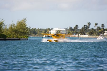 small yellow seaplane taking off close to shore
