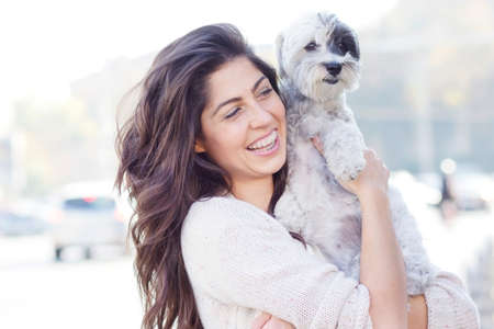 Young beautiful woman smiling and hugging her small poodle dog on the street