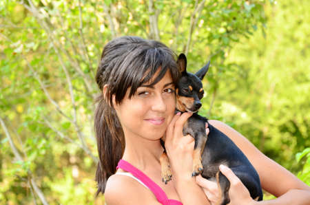 Young beautiful woman smiling and hugging her small black pincher dogの写真素材