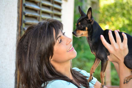 Young beautiful woman smiling and hugging her small black pincher dogの写真素材