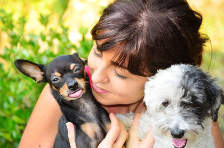Young beautiful woman smiling and hugging her small black pincher dog and a white poodle