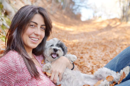 smiling woman laying in the autumn forest with her small poodle dogの写真素材
