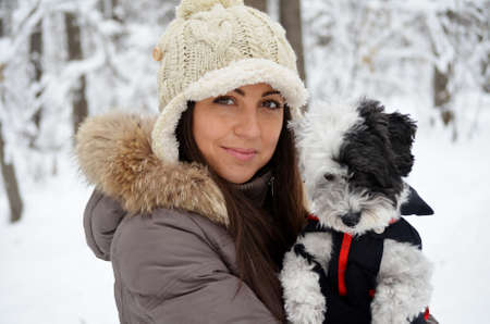 Young beautiful woman smiling and hugging her dressed white poodle dog.Winter timeの写真素材