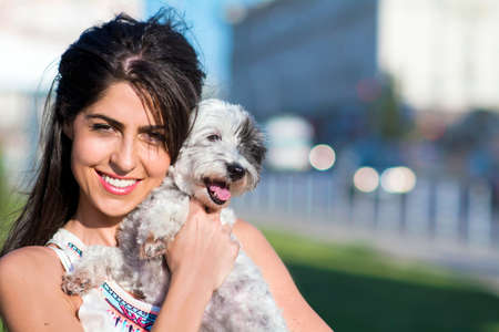 Young beautiful woman smiling and hugging her small poodle dog on the streetの写真素材