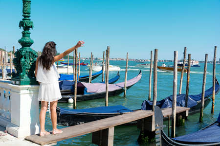 beautiful young tourist woman enjoying the venetian view with gondolas floating in the blue seaの写真素材