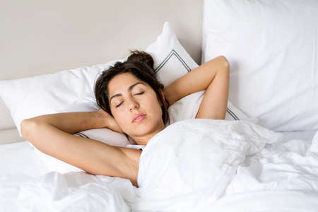 young woman happily sleeping in white bedの写真素材