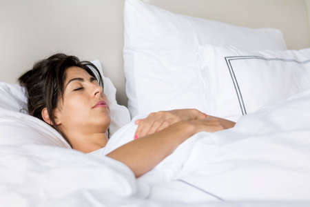 young woman happily sleeping in white bedの写真素材