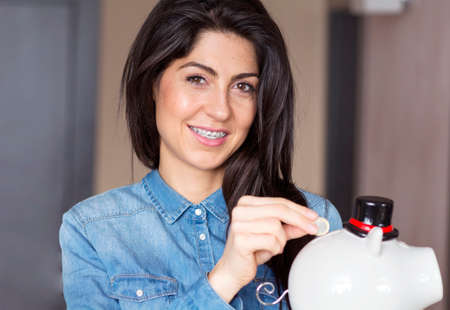 Woman Putting money In Piggy Bank, Indoorsの写真素材