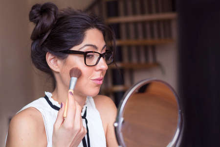 young beautiful woman applying her make-up with a big brush , looking in a mirrorの写真素材