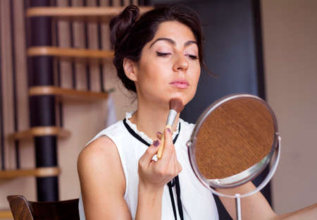young beautiful woman applying her make-up with a big brush , looking in a mirrorの写真素材