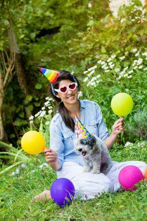 happy young woman celebrating birthday with her dog ,balloons and hats in a summer gardenの写真素材