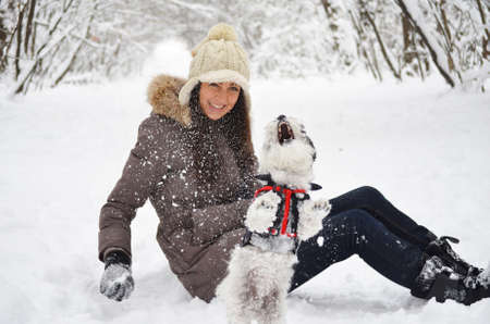 Young beautiful woman smiling and hugging her dressed white poodle dog.Winter timeの写真素材