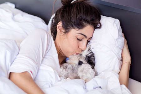 beautiful young  woman sleeping with her small poodle dog in a bedの写真素材