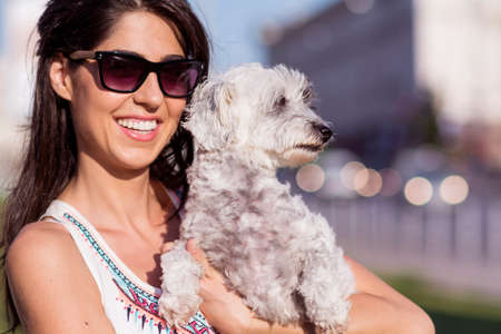 Young beautiful woman smiling and hugging her small poodle dog on the streetの写真素材