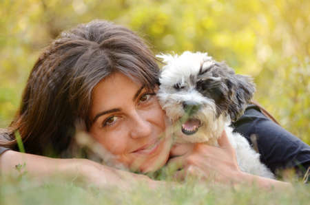 smiling woman laying on a meadow with her small havanese dog