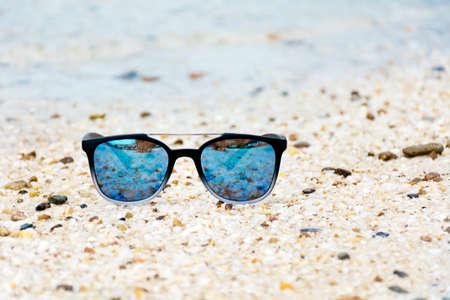 Fashion blue sunglasses on sandy  beach near the blue sea. Summer holiday conceptの写真素材