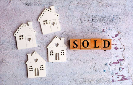 Sold word on wooden cubes and miniature houses on gray textured  background . Housing conceptの写真素材