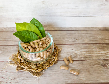 Pills in a glass jar with green leaves on a wooden backgroundの写真素材