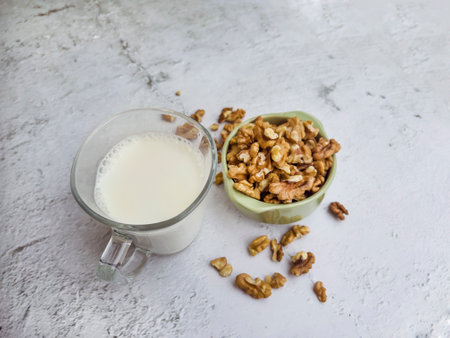 A glass of milk and a bowl of walnuts on a white backgroundの写真素材