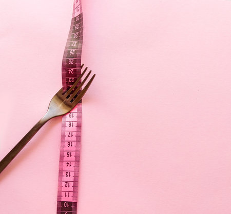 Fork and measuring tape on a pink background. Diet concept.の写真素材