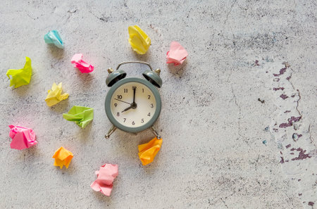 Alarm clock and colorful crumpled paper balls on concrete backgroundの写真素材