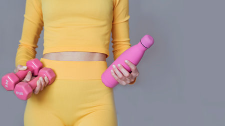 Young woman in yellow sportswear with dumbbells on gray backgroundの写真素材