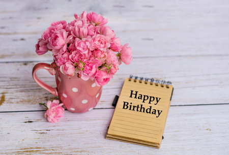Happy birthday card with pink roses in a cup on white wooden backgroundの写真素材