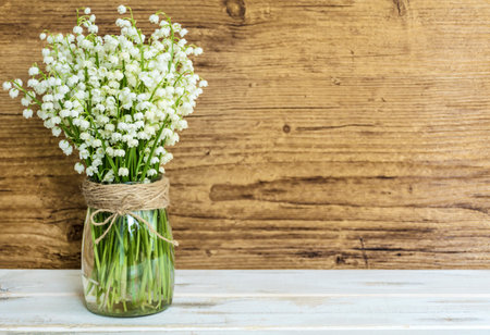 Lily of the valley in a glass vase on a wooden backgroundの写真素材
