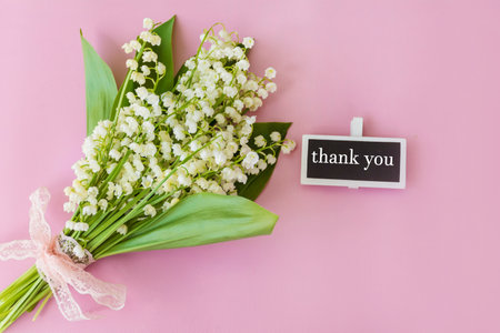 Lily of the valley flowers on pink background with blackboard with thank you messageの写真素材