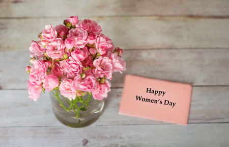 Bouquet of pink roses in a glass vase and greeting card with text Happy Women's Dayの写真素材