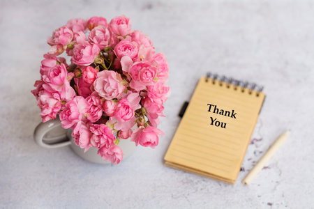 Vase with pink roses and notebook with thank you text on tableの写真素材