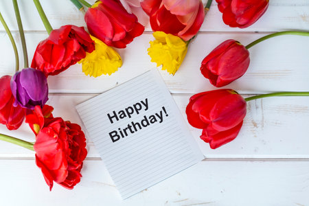 Happy birthday card with red and yellow tulips on white wooden backgroundの写真素材