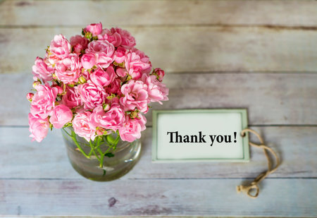 Bouquet of pink roses in a glass vase and a card with the text thank youの写真素材