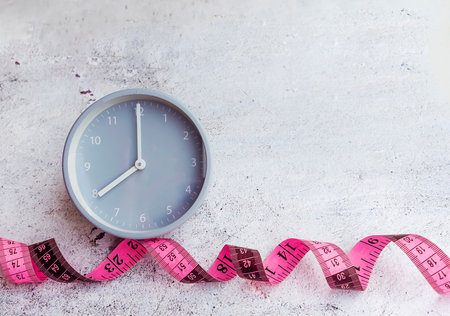 Time for diet and weight loss concept with clock and measuring tape on concrete background