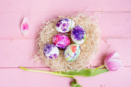 Easter eggs in a nest with tulips on a pink wooden background