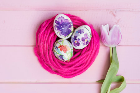 Easter eggs and tulips on pink wooden background. Top view