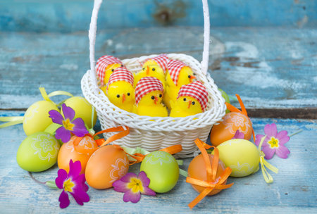 Easter basket with colorful eggs and chickens on blue wooden background.の写真素材