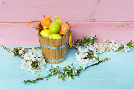 Easter eggs in basket and blooming branch of cherry on wooden backgroundの写真素材